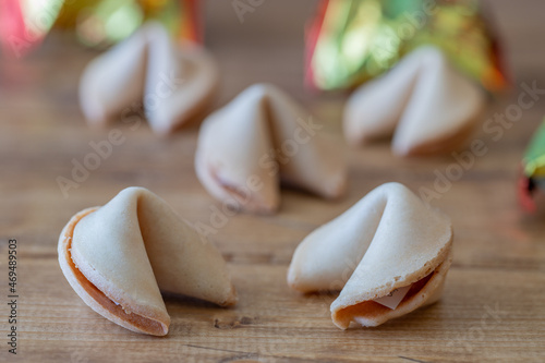 Five closed chinese fortune cookies on a wooden table with the packaging in the background, focus on foreground