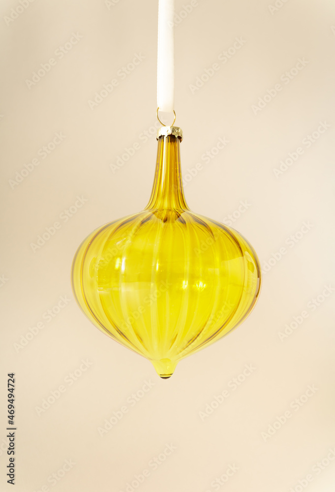Christmas vintage shiny vivid yellow glass ornament hanging on white rope behind pastel beige champagne colour background. Minimal winter holidays and New Year layout. Retro 80s or 90s aesthetic.