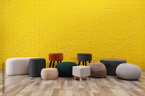 Different stylish poufs and ottomans near yellow brick wall, space for text