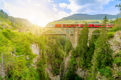 Red train crossing the Solis Viaduct bridge of Swiss railway in Switzerland to Pontresina town. Swiss train Bernina in Grisons at sunset. Albula Railway section between Thusis and Tiefencastel photo
