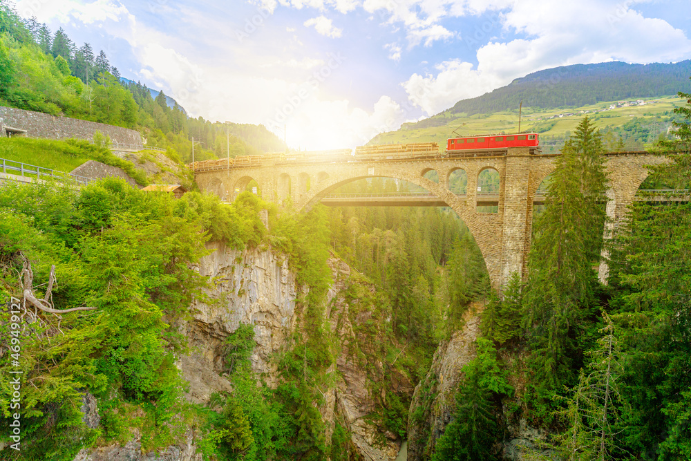 Sunset travel of a Swiss red train crossing the Solis Viaduct bridge of Switzerland railway. Swiss train Bernina in Grisons at sunset. Albula Railway section between Thusis and Tiefencastel.