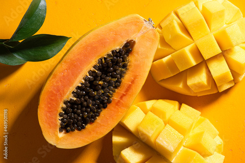 Papaya and mango tropical fruits on yellow background flat lay with natural sun light and shadows photo