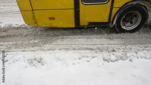 Wheels of a yellow bus ride in slow motion on a snowy road. 