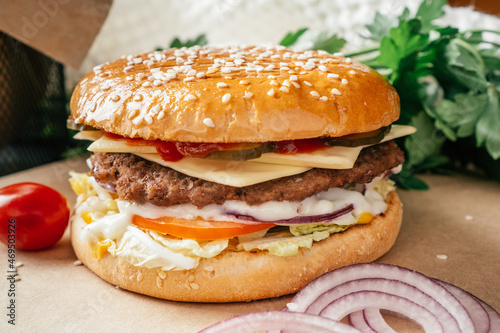 Classic double burger with meat cutlet, lettuce, tomato, pickled cucumber, cheese, onion and sauce on craft paper