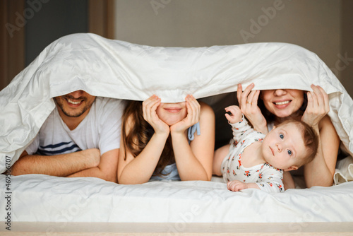 the family is at home in bed under a blanket, only smiles and a small baby are visible