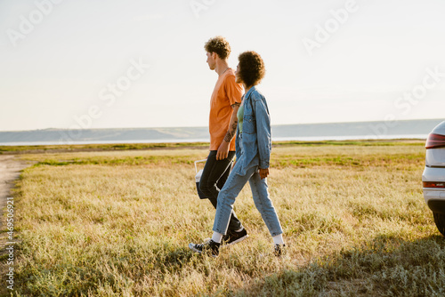Multiracial couple walking with cooler bag on field during car trip © Drobot Dean