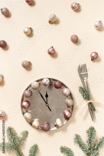 Winter festive table setting concept, Christmas plate with clock hands show twelve or midnight, sparkle balls beige pink color, knife, fork, fir tree branches. New Year holiday food concept