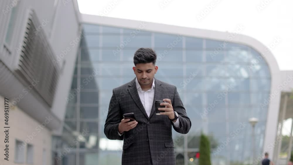 Young handsome Indian businessman standing in front of modern building or airport, smiling and talking on cell phone, drinking take away coffee Young handsome Indian businessman standing in front of modern building or airport, smiling and talking on cell phone, drinking take away coffee