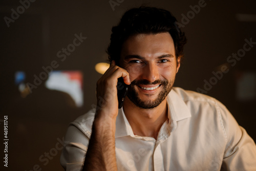 White bearded man smiling and talking on cellphone in office