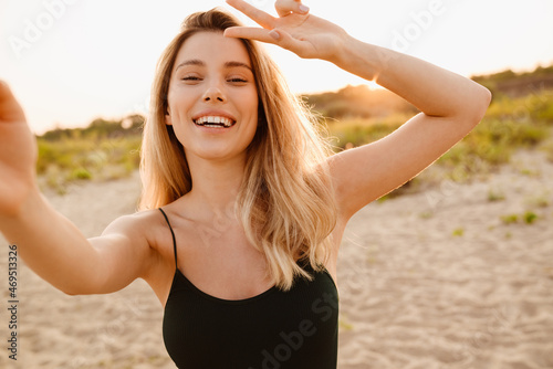 Young blonde woman gesturing while taking selfie photo