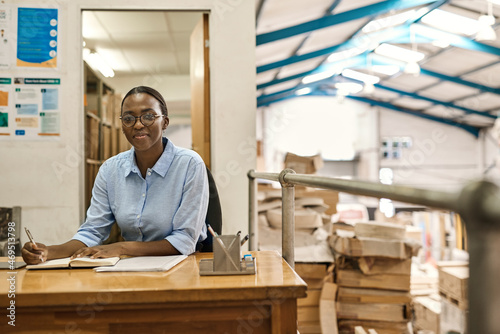 Smiling young African woman working at her desk in a warehouse © mavoimages
