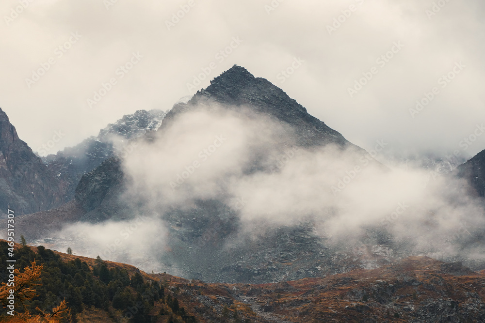 Morning mountain background. Dramatic fog among giant rocky mountains. Ghostly atmospheric view to big cliff. Low clouds and beautiful rockies. Minimalist scenery mysterious place.