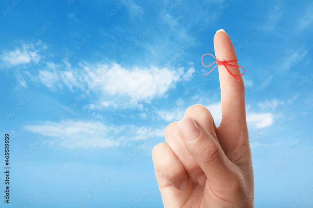 Woman showing index finger with tied red bow as reminder against blue sky, closeup Woman showing index finger with tied red bow as reminder against blue sky, closeup