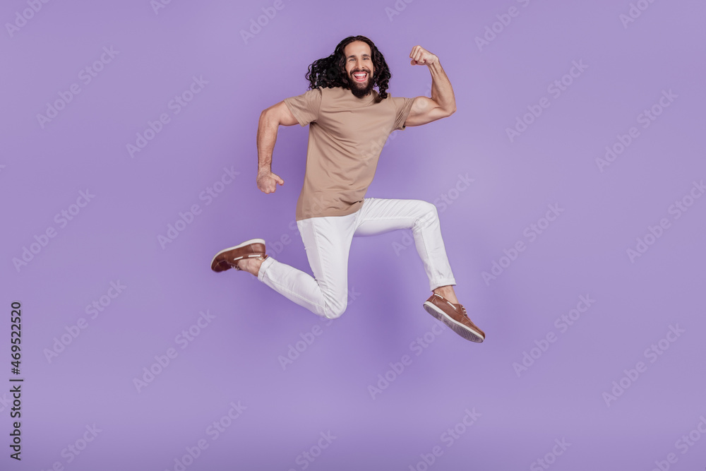 Full body profile side photo of young cheerful man sporty biceps training jump isolated on purple color background Full body profile side photo of young cheerful man sporty biceps training jump isolated on purple color background