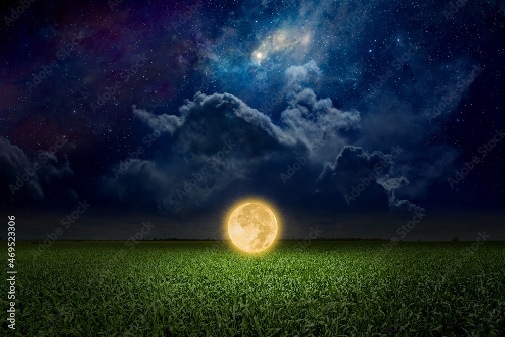 Unreal fantastic image - luminous sphere, similar to full moon, levitates over green field. Bright stars, glowing nebula and clouds in dark blue sky.