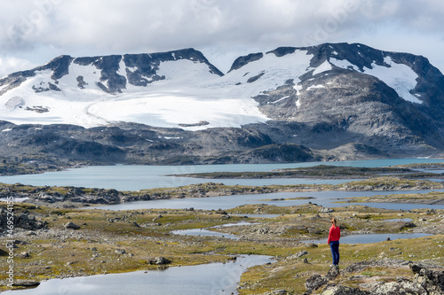Lone hiker looking at spectacular glacier with surrounding lakes and mountains, showcasing Norway’s icy landscapes. 