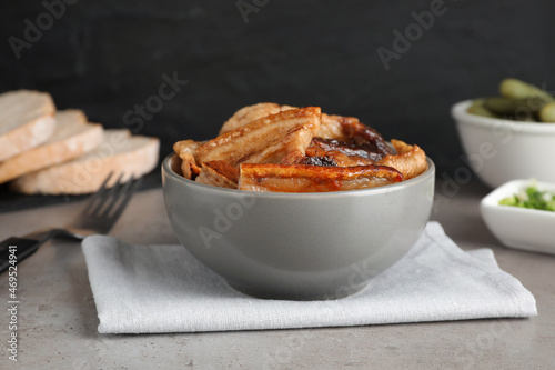 Bowl with tasty fried pork fatback slices on grey table