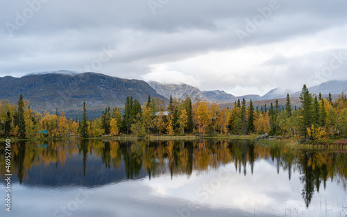 Tranquil Lakeside Reflection in Swedish Autumn. Perfect mirror image of the surrounding autumnal trees on the calm waters of a secluded Swedish lake.