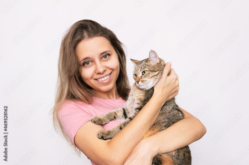 A young beautiful smiling blonde woman holding a young adorable Tabby cat in her hands isolated on a white background. Good friends. Friendship of a pet and its owner. Cuddles