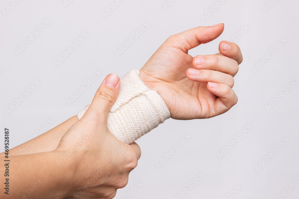 Cropped shot of a young woman holding a bandaged wrist in her hand isolated on a gray background. Wrist injuries, arm pain, carpal tunnel syndrome, neuralgia Cropped shot of a young woman holding a bandaged wrist in her hand isolated on a gray background. Wrist injuries, arm pain, carpal tunnel syndrome, neuralgia