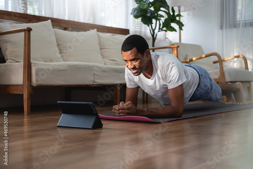 African American male using digital tablet while doing plank exercise © eggeeggjiew