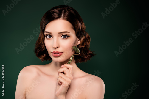 Photo of good mood smiling female using mezoroller on face lifting spa procedure isolated on green color background photo