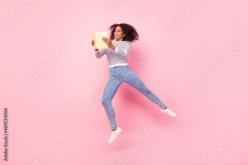 Full length portrait of attractive carefree girl hold book jump dream isolated on pink color background