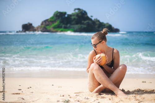 Happy white Caucasian girl on the beach with a coconut in her hands on the background of the ocean and islands