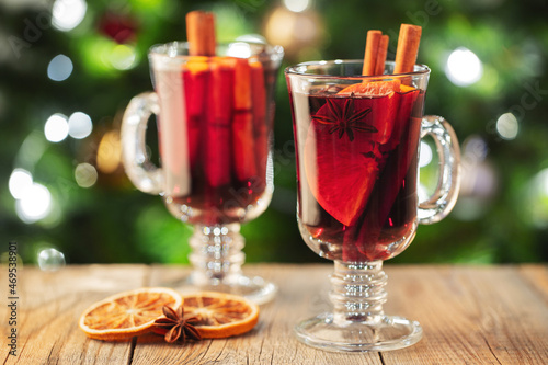 Two glass of christmas mulled wine or gluhwein with spices and orange slices on rustic table against the Christmas tree. Traditional drink on winter holiday
