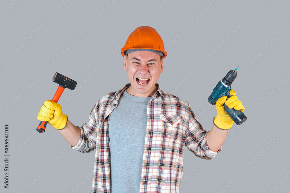 An angry construction worker in hardhat screams with a tool in his hands holding a screwdriver and a hammer An angry construction worker in hardhat screams with a tool in his hands holding a screwdriver and a hammer