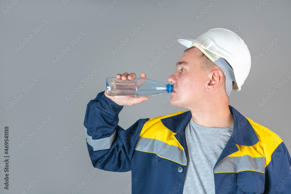 A construction worker in a white helmet and work clothes drinks water from a plastic bottle A construction worker in a white helmet and work clothes drinks water from a plastic bottle