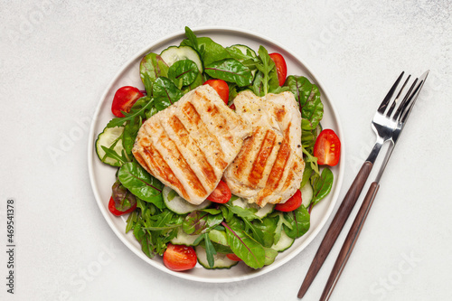Fresh salad - cucumbers, tomato, arugula, chards leaves and chicken fillet grill in a plate on the table. Top view. Healthy diet food.