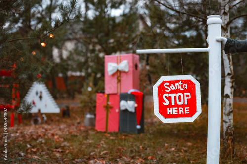 Outdoor road barrier in Christmas decorations in pine trees with the inscription Santa, please stop here.