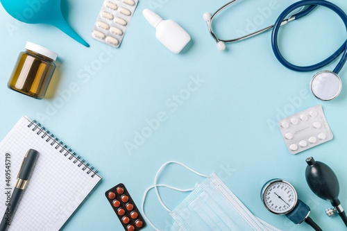 Medical concept, flat lay on blue background. Copy space in center. Stethoscope, tonometr, pills and other medical equipment on blue, top view