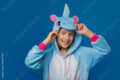 a pretty girl in a cozy blue unicorn costume poses in the studio on a blue isolated background. Place for text