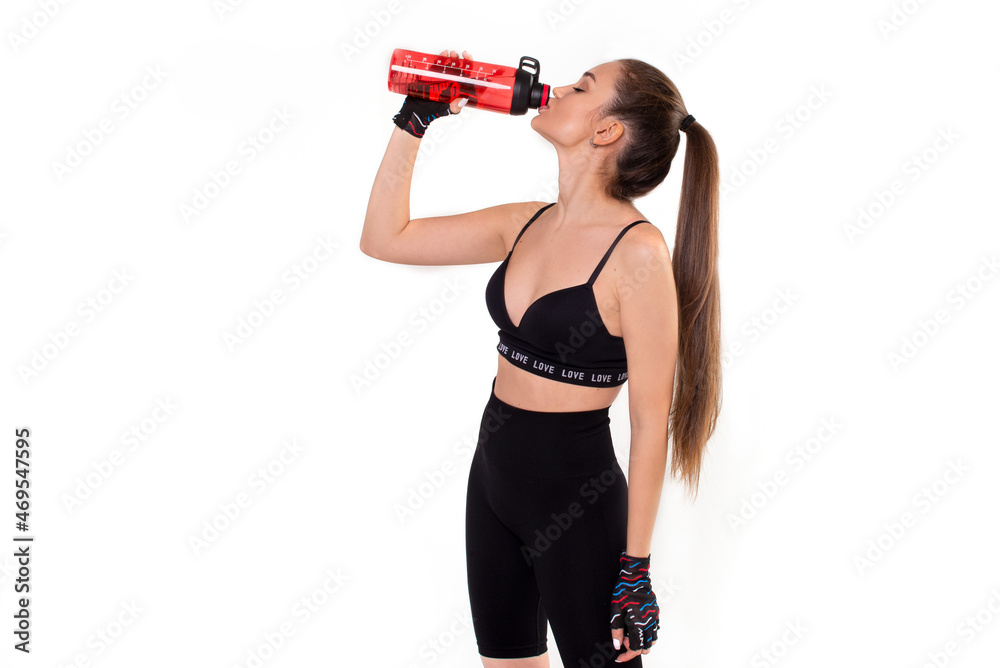 Girl athlete drinks from a red sports bottle on a white background Girl athlete drinks from a red sports bottle on a white background