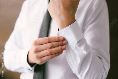 Man in a tie buttons up the sleeves of a white shirt. Close-up