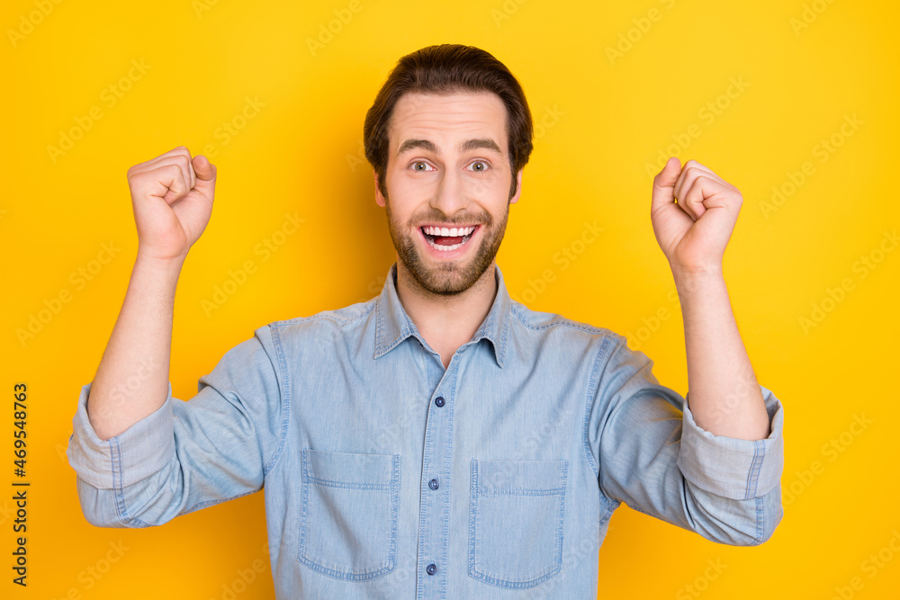 Fototapeta premium Photo portrait of young man smiling gesturing like winner wearing denim shirt isolated on bright yellow color background