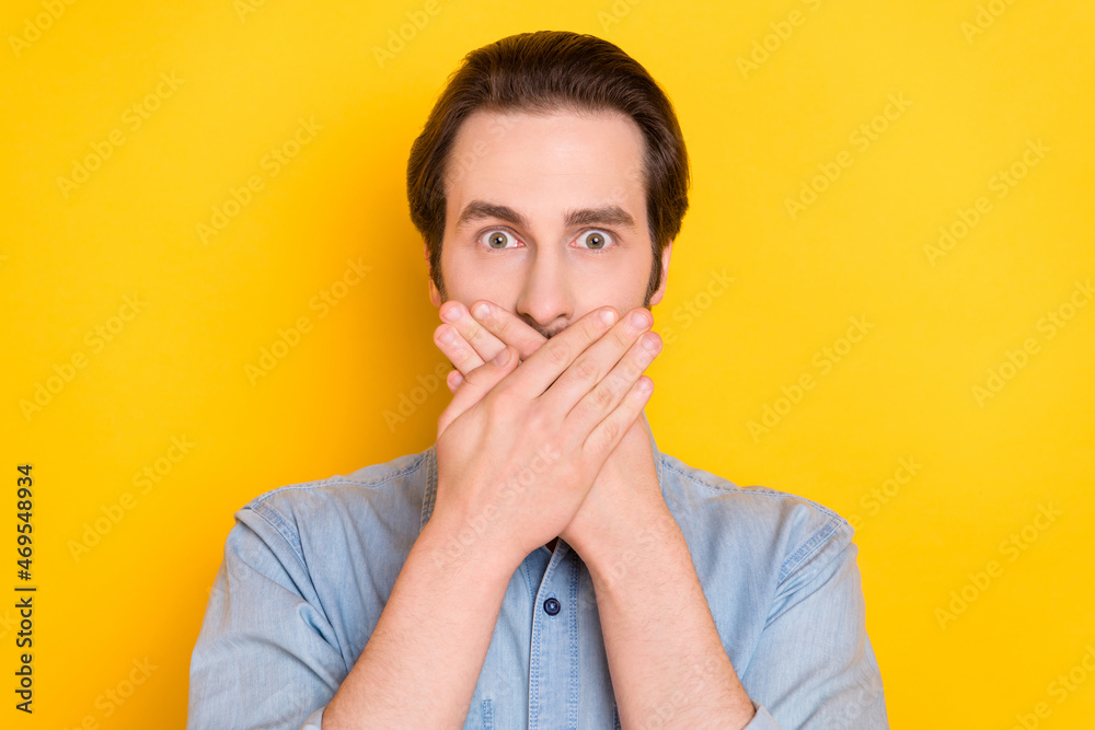 Photo portrait of young man covered mouth with hands keeping secret isolated on vivid yellow color background Photo portrait of young man covered mouth with hands keeping secret isolated on vivid yellow color background