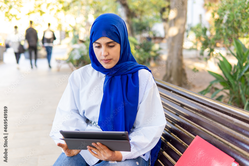 Young muslim woman wearing hijab using a tablet sitting in the university campus Young muslim woman wearing hijab using a tablet sitting in the university campus