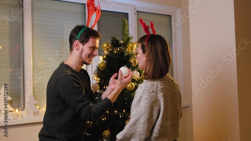 Young couple decorating their christmas tree at home, having fun together and enjoy the winter holidays.
