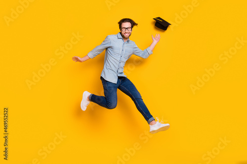 Full body profile side photo of young man happy positive smile fly air fall mortarboard jump up isolated over yellow color background