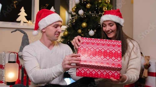 Beautiful young couple opening a gift box and smiling, enjoy the winter holidays near the Christmas tree.