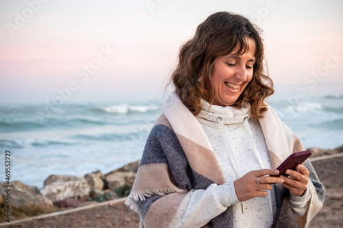 Happy baby  boomer woman with a blanket on the beach looking at her mobile phone photo