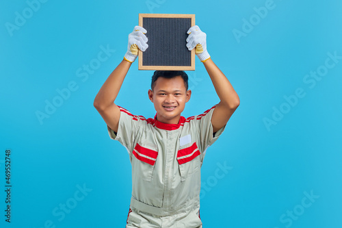 Portrait of cheerful young Asian mechanic showing blank board over blue background