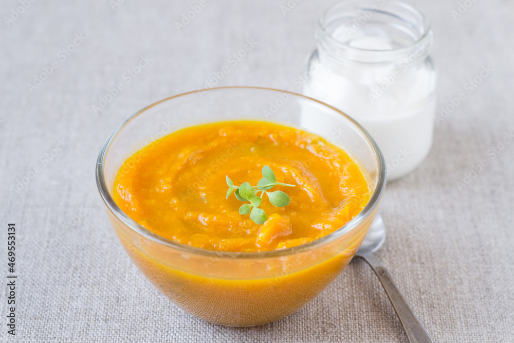 Pumpkin cream soup in a glass bowl and sour cream