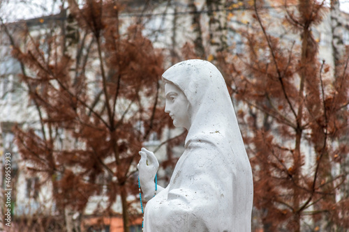 White concrete sculpture of the monument to the Mother of God in the park. Cross road near the church