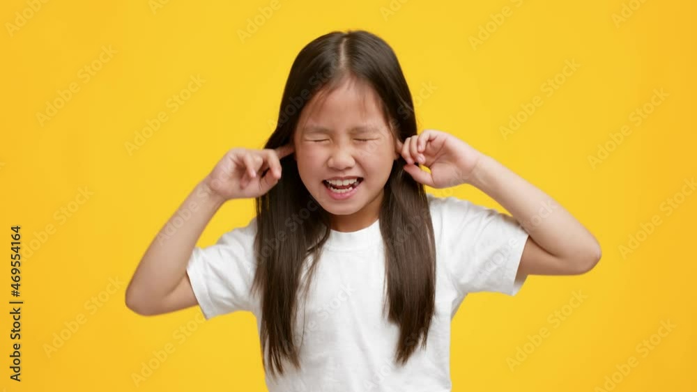 Naughty Little Asian Girl Plugging Ears With Fingers, Yellow Background