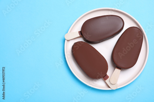Plate with glazed ice cream bars on light blue background, top view. Space for text