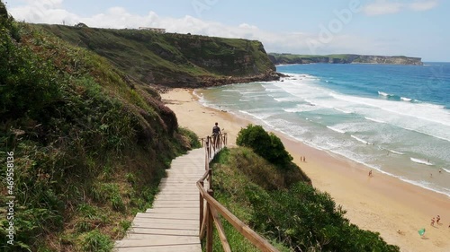 Descending a wooden steps to a beautiful sandy beach. Blue sea and long waves. Steep cliffs on the ocean coast. Wonderful walk along the ocean. Cantabria. Asturias. Camino de Santiago. Pilgrim.
